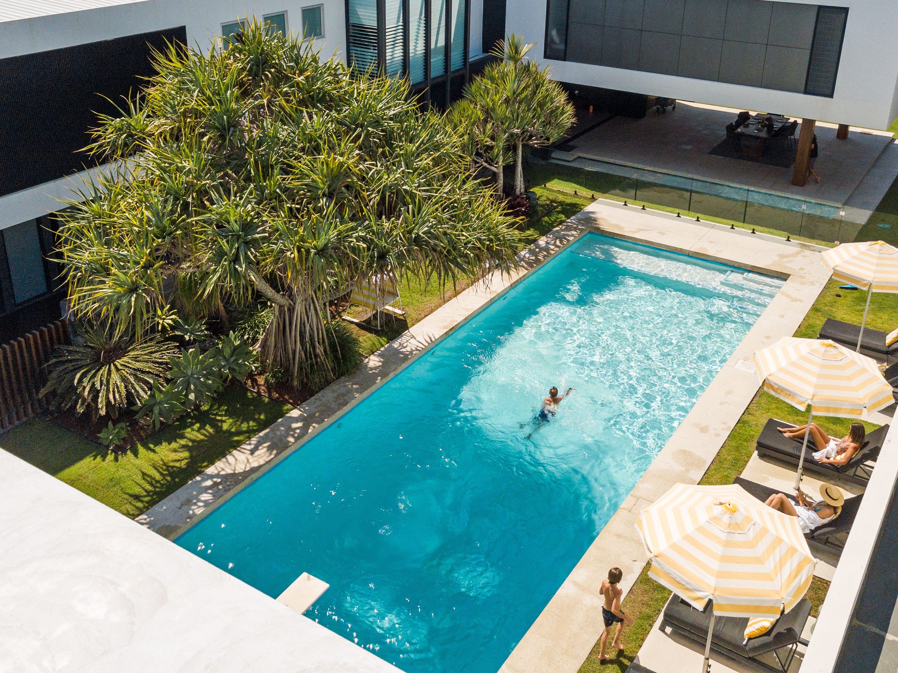 Aerial view of a luxurious pool surrounded by tropical plants and sun lounges with striped umbrellas, showcasing guests enjoying the serene environment.